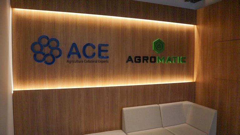 Recepção do escritório Agromatic com os logos Agromatic e ACE iluminados em painel de madeira