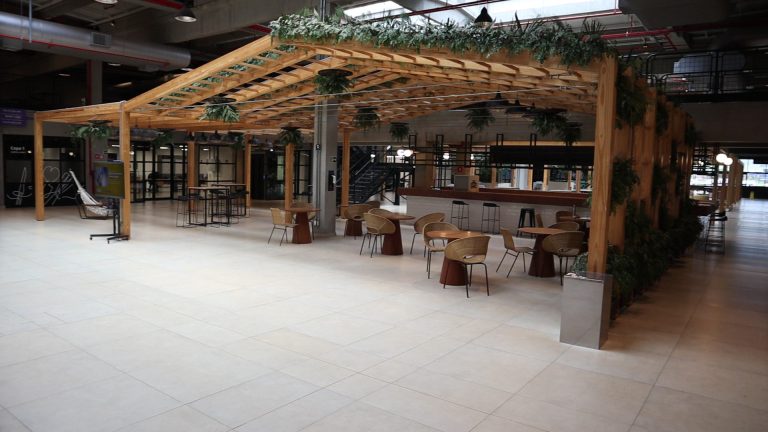 Espaço de convivência com pérgola de madeira, mesas e café compartilhado